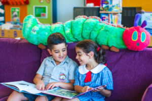 Two students smiling and reading a book together on a couch